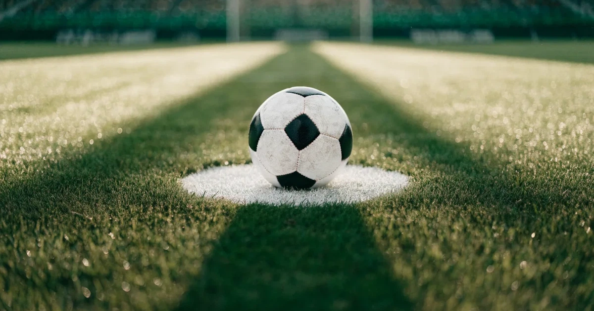 Uma bola de futebol no ponto central de um relvado, à luz da manhã